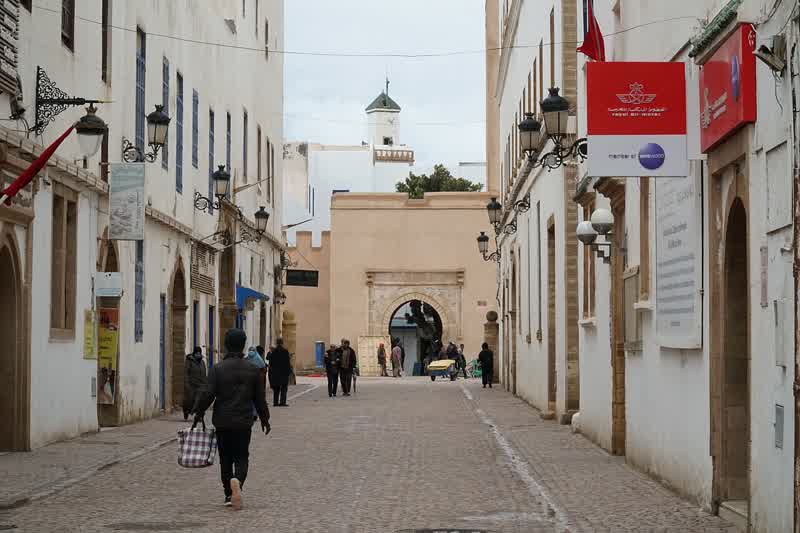 A stone archway leading into a narrow street in Essaouira's medina, the planned grid visible in the straight axis ahead