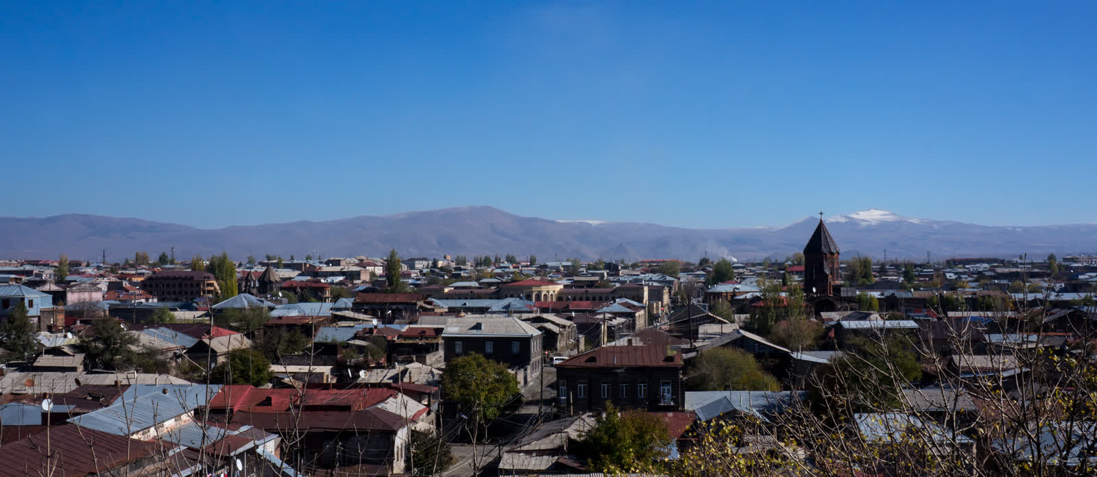 Panoramic view of Gyumri, Armenia, showing the dense stone architecture of the old city with church spires and snow-capped mountains in the background