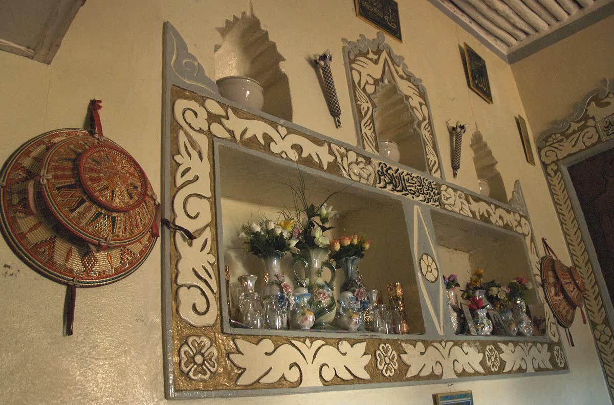 Interior wall of a traditional Harari house: carved and painted plaster niches holding porcelain and glassware, with woven basketry hung alongside.