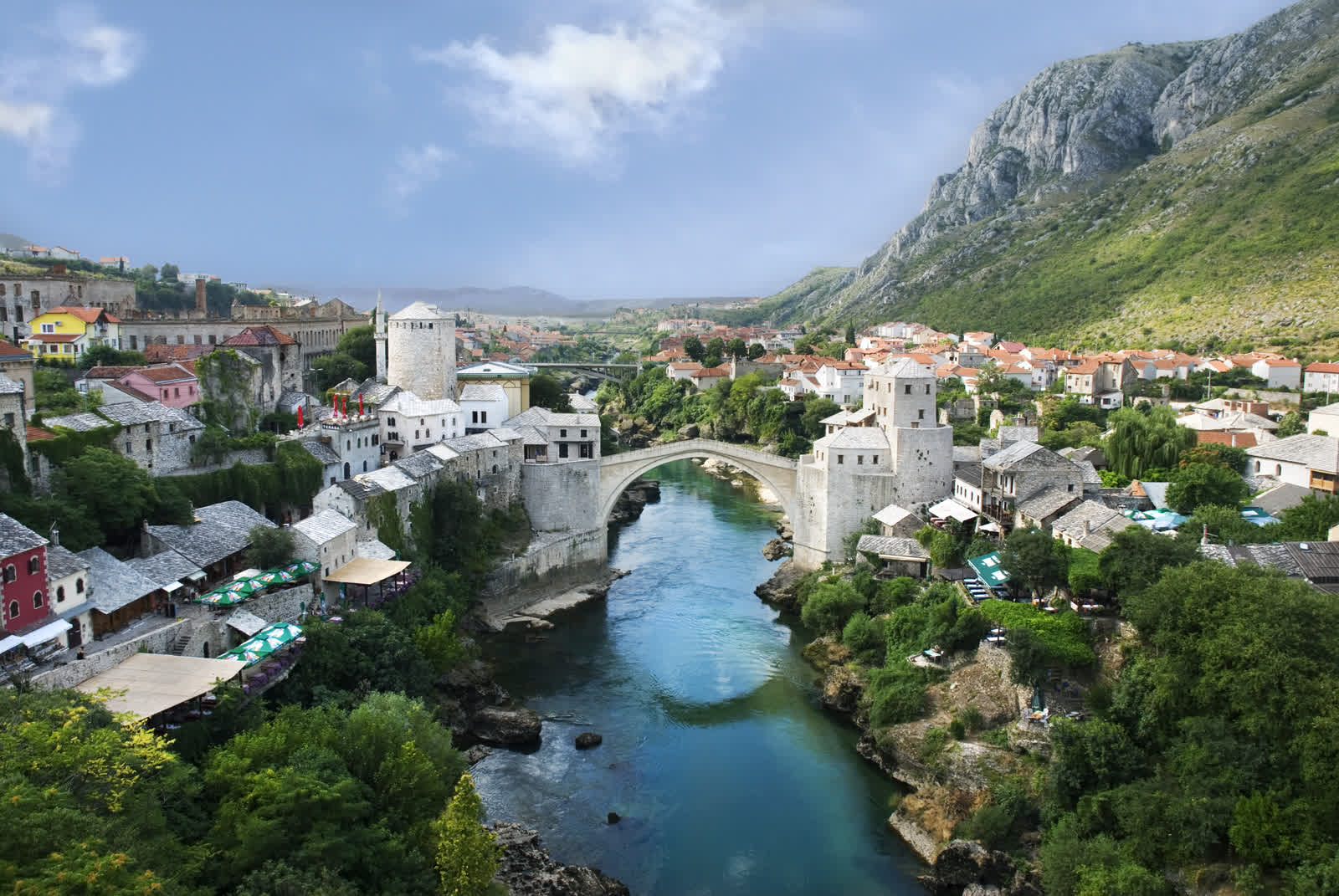 Panoramic view of Mostar's Old Town showing the Stari Most arch bridge spanning the emerald Neretva River, flanked by Ottoman-era stone buildings