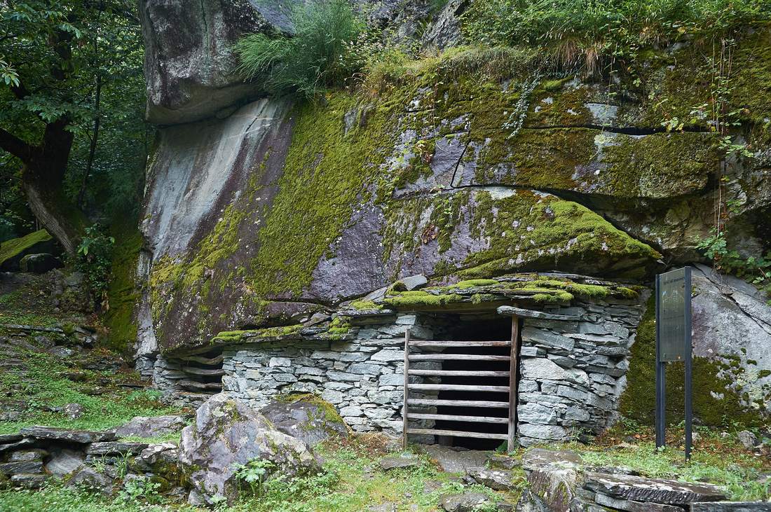 A historic stone stable built under an overhanging boulder in Val Bavona, the rock face serving as the roof