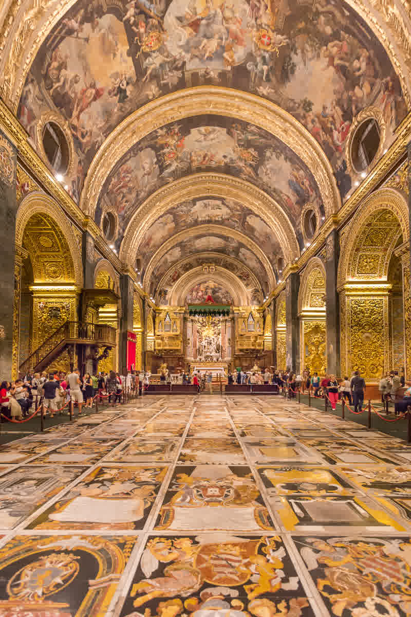 The nave of St. John's Co-Cathedral, Valletta, showing the polychrome marble tomb-slab floor and baroque gilded interior